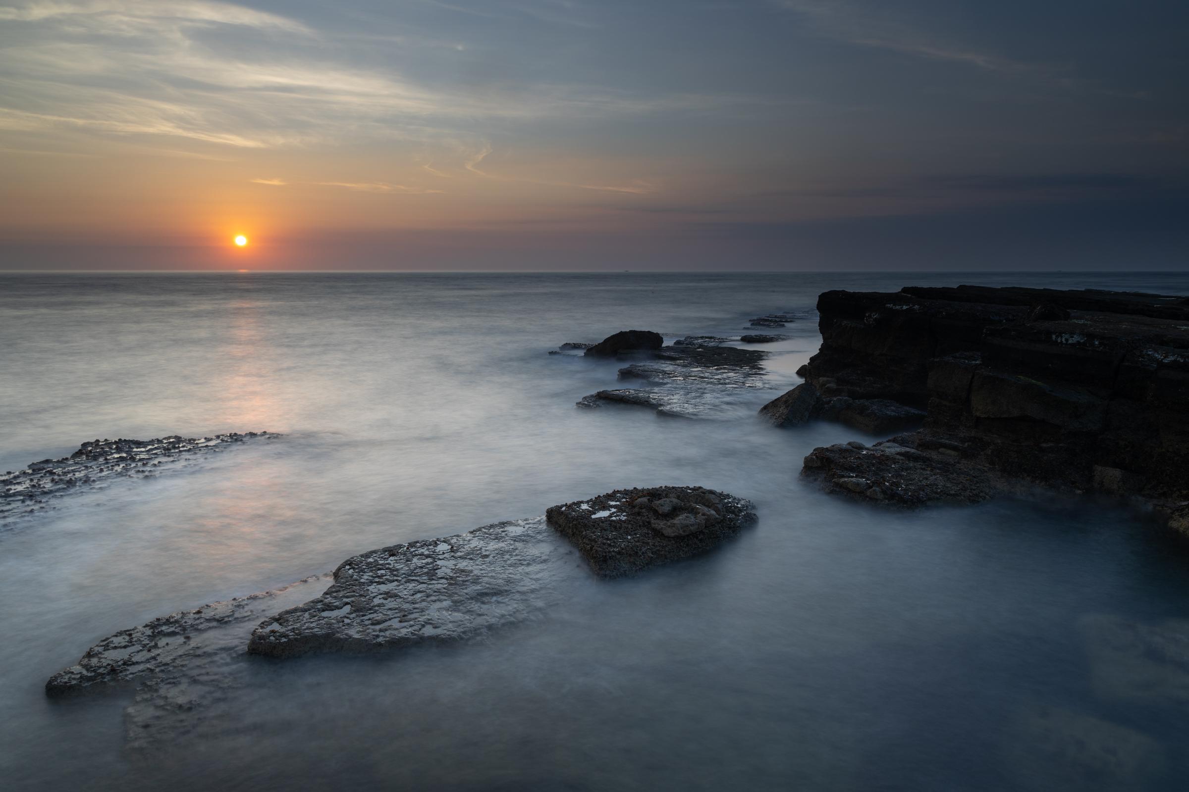 Filey Brigg at sunrise on a hazy summer day, captured with a long exposure to capure the milky motion of the rising tide as it ebbs and flows.