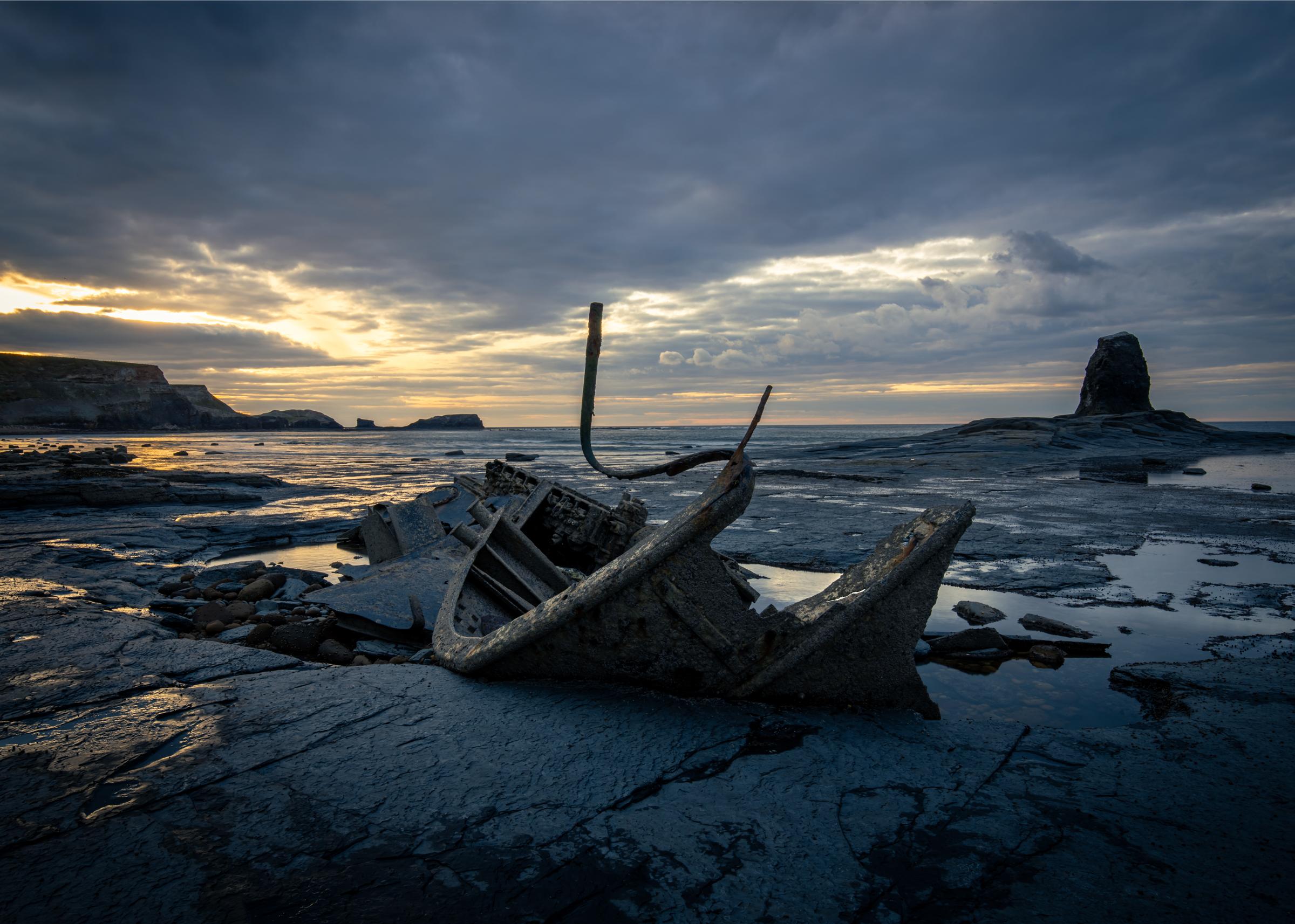 Moody sunset at Saltwick Bay near Whitby, with the wreck of Admiral Van Tromp in the foreground, Black Nab in the middle ground on the right and in the distant, in the glow of the setting sun, Saltwick Nab.