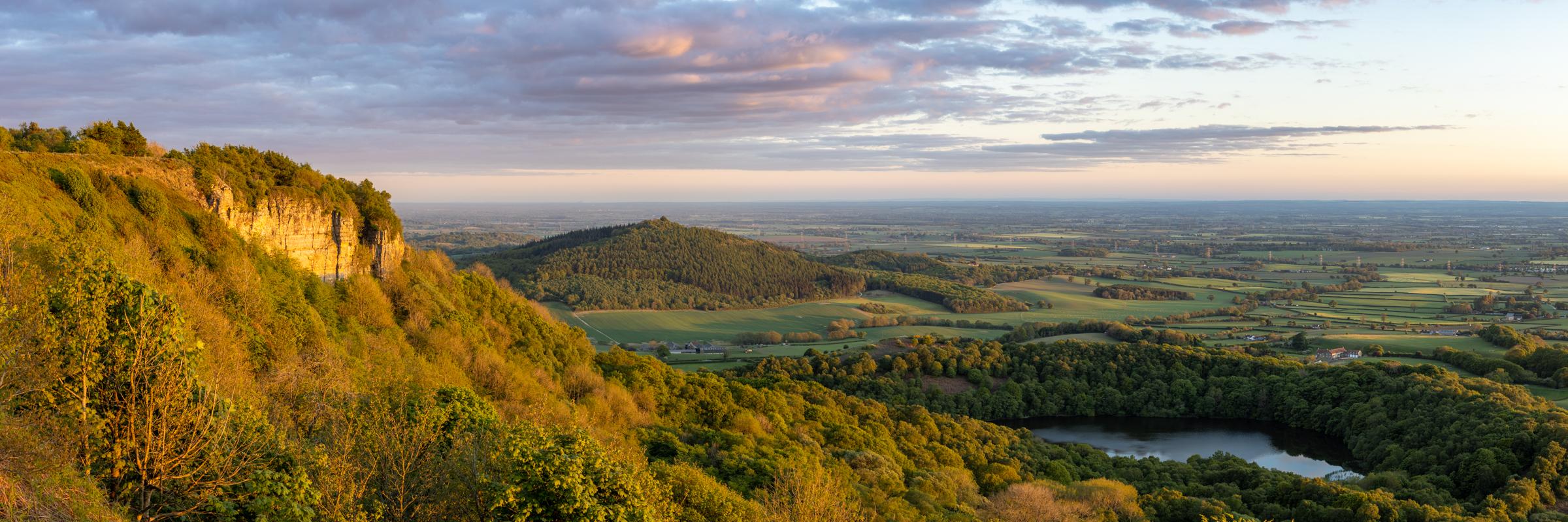 Panoramic looking towards Hood Hill with Garbutt Wood, Goremire Lake and Whitestone Cliff drenched in the evening golden light